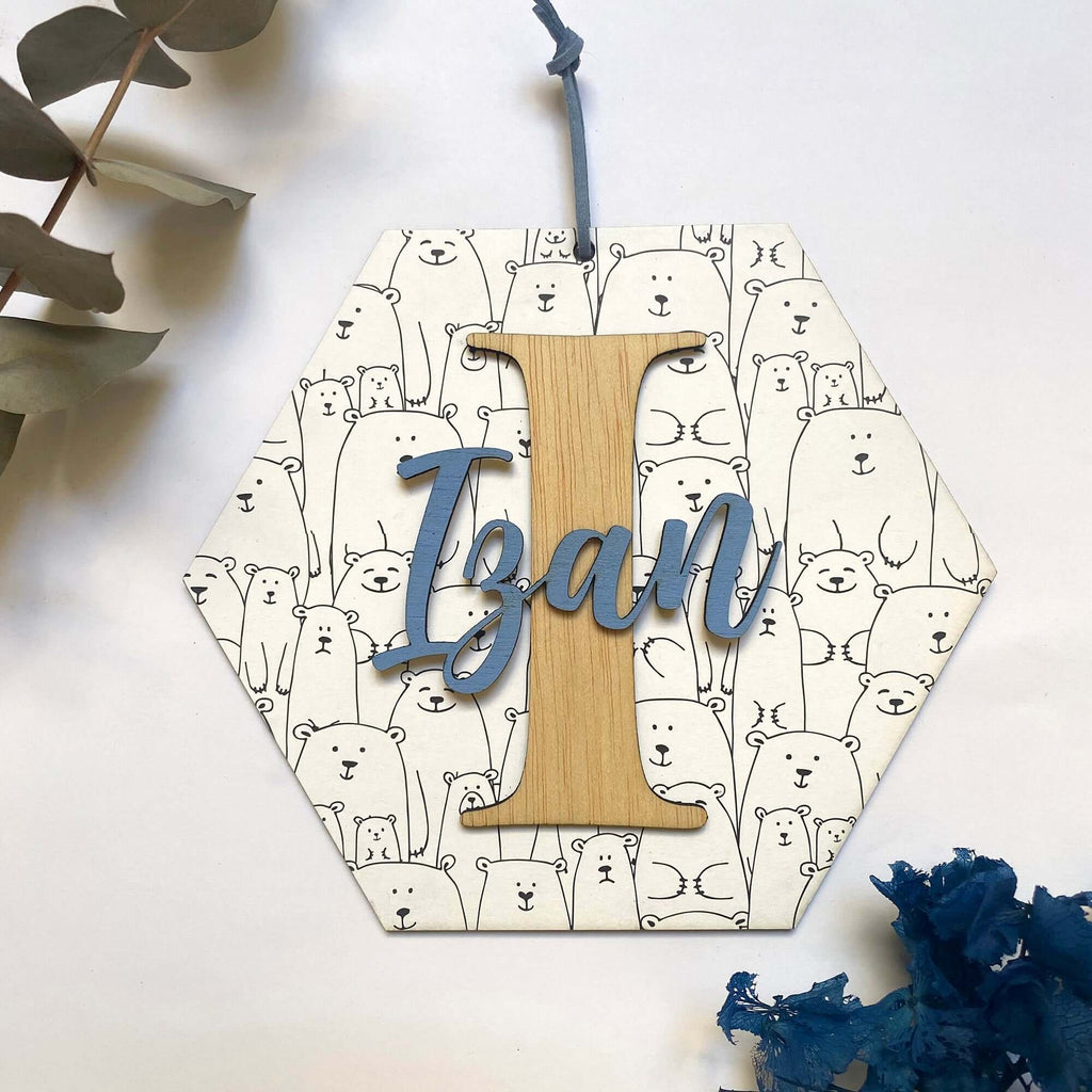 Hexágono en madera con una base de papel decorado y una inicial en el que reposa el nombre de un niño.